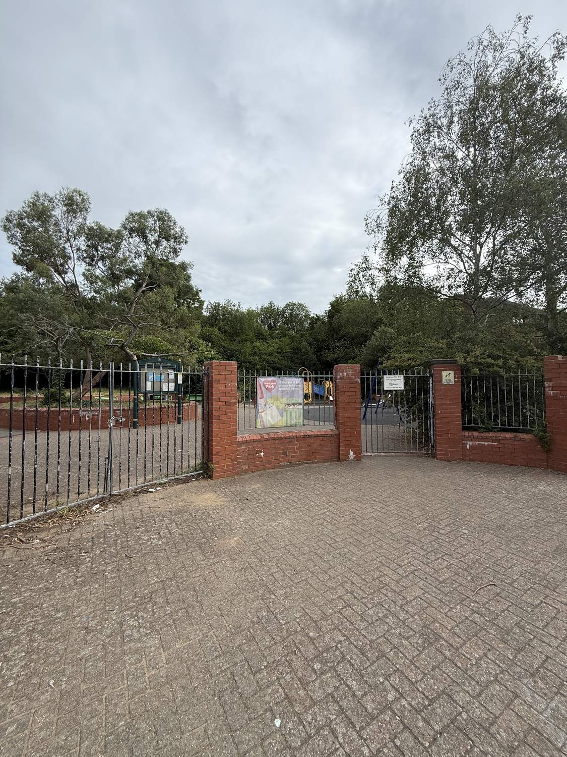 The locked entrance gates and brick walls of Rainbow Park at Rusper Close, with the empty play area behind.