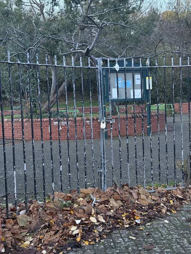 A padlock on the park gate beside a low boundary wall.
